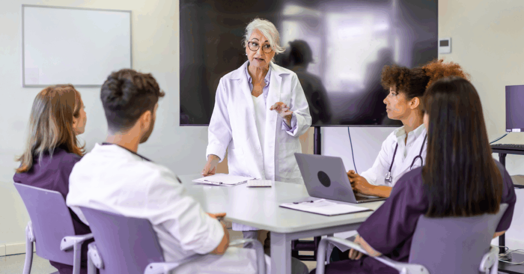 Clinical instructor guides staff at a table with laptop and display – integration training for healthcare teams on HL7/FHIR basics.